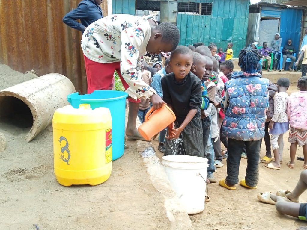 Children lining up with containers to collect water at the Centre